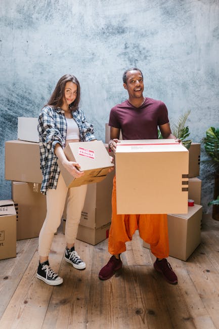 Two movers inside a residential property engaged in a house relocation process. The female mover is wearing casual clothing, including a checkered shirt, light-colored trousers, and sneakers, and is h